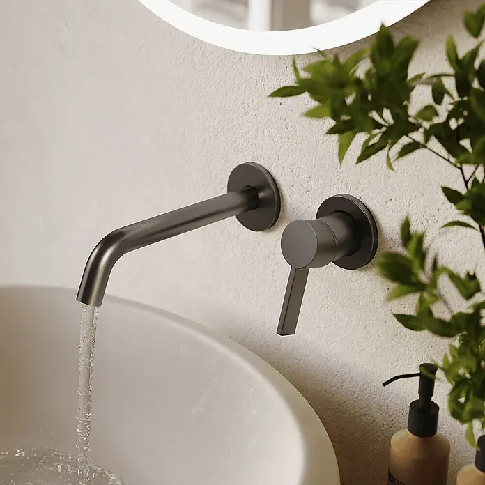 LOMAZOO Waschtischarmatur LMZ-GAIA - Gunmetal - Dunkle Metall-Wandarmatur mit Wasser, das in ein weißes Waschbecken fließt.