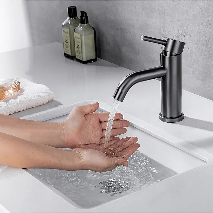 LOMAZOO Waschtischarmatur LMZ-MACY - Gunmetal - Mattschwarzer Wasserhahn mit fließendem Wasser in ein weißes Waschbecken, Hände fangen Wasser auf.