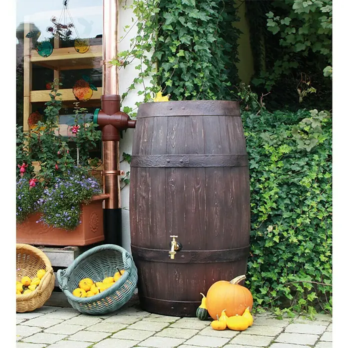 Arves Regenspeicher Barrique - 250 l, Dunkelbraun - Eine Regentonne in Holzoptik mit Messinghahn und dazugehörigen Kürbissen, ergänzt durch Körbe, Pflanzen und ein Fallrohr.
