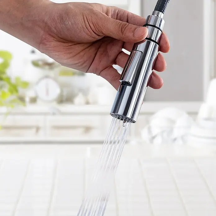 LOMAZOO Spültischarmatur YJ-PSWK-BLL9 - Chroom - Eine Hand hält einen verchromten ausziehbaren Küchenarmatur-Brausekopf, aus dem Wasser sprüht, vor unscharfem Küchenhintergrund.