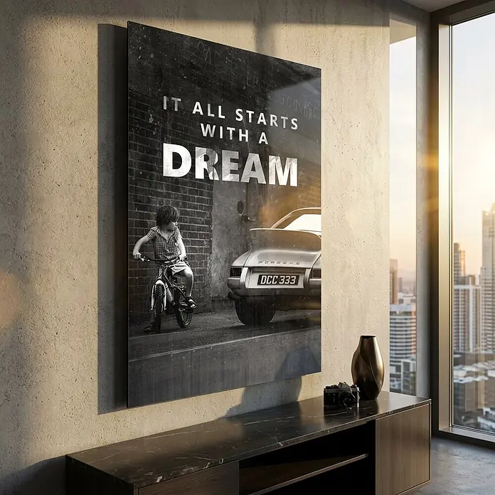 Dotcomcanvas Decopanel - It All Starts with a Dream, B x H: 58 x 90 cm - Schwarz-weißer Inspirationsdruck mit Kind auf Fahrrad neben Porsche und Text 'IT ALL STARTS WITH A DREAM', an einer Wand in einem modernen Raum.