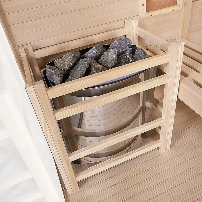 Artsauna Elementsauna Vantaa - L x B x H: 140 x 175 x 200 cm - Saunaofen mit dunkelgrauen Saunasteinen, geschützt durch ein helles Holzgitter, in einer Holzsauna.