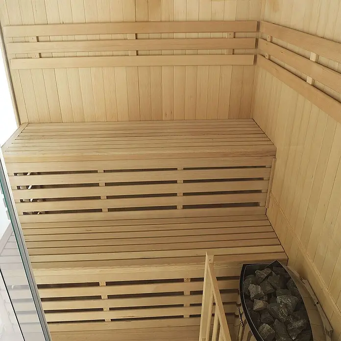 Artsauna Elementsauna Espoo - L x B x H: 150 x 150 x 200 cm - Sauna-Innenraum aus hellem Holz mit mehrstufigen Lattenbänken und einem steinbefüllten Ofen.