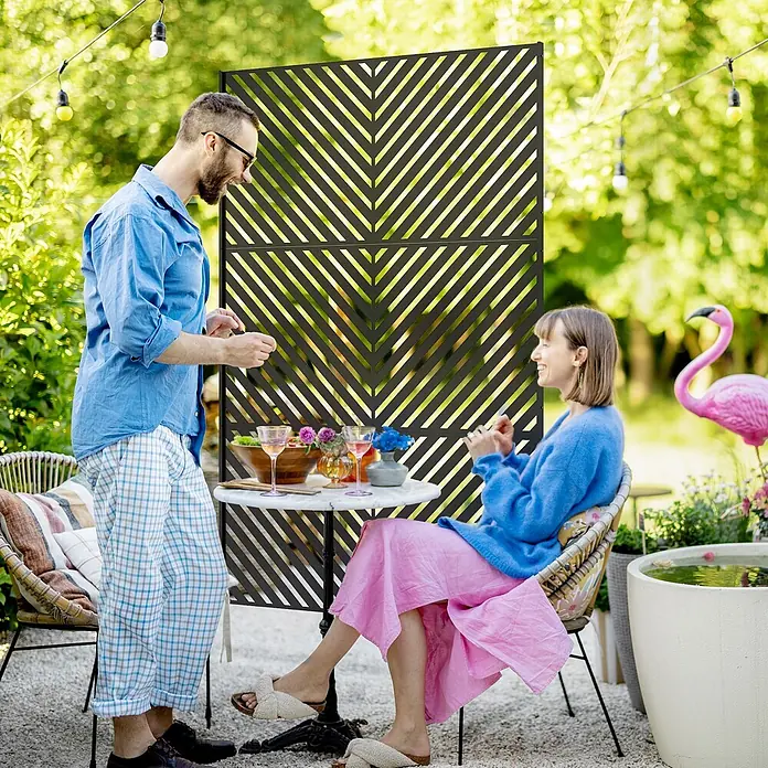 Outsunny Sichtschutzelement - Stahl, Schwarz - Dunkler, dekorativer Sichtschutz mit diagonalem Chevron-Muster, der einen gemütlichen Gartensitzbereich abtrennt.
