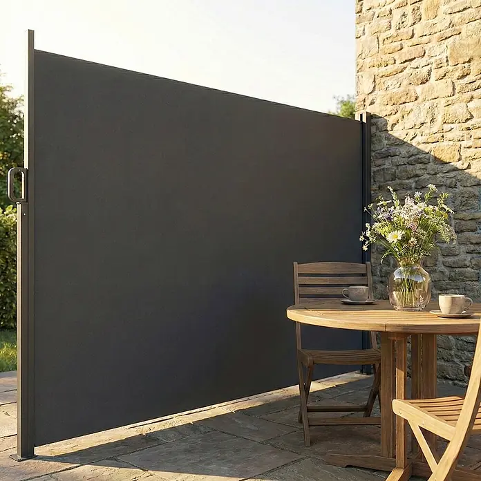Outsunny Sichtschutzelement - Aluminium, Dunkelgrau - Dunkelgraue ausziehbare Seitenmarkise auf einer Terrasse, die Sichtschutz an einer Steinmauer mit Sitzgelegenheiten bietet.