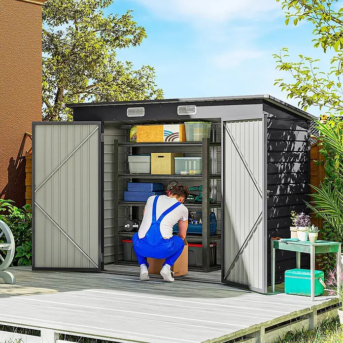 Outsunny Gerätehaus - Außenbreite inkl. Dachüberstand: 249 cm, Außentiefe inkl. Dachüberstand: 121 cm, Stahl, Grau - Ein Mann räumt Gegenstände in einem großen, dunkelgrauen und hellgrauen Metall-Gartenschuppen mit Regalen auf einer Holzterrasse in einem sonnigen Garten.