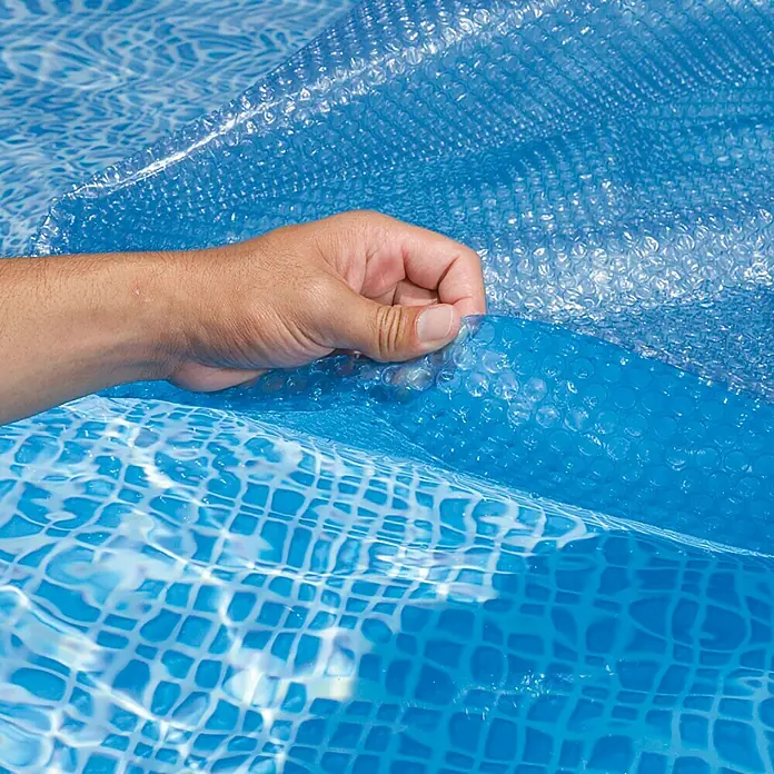 myPool Solarabdeckplane - Durchmesser: 460 cm, Passend für: Rundbecken bis Ø 460 cm - Nahaufnahme einer blauen Poolfolie, die auf einem Schwimmbecken liegt und von einer Hand angehoben wird, um die darunterliegende Oberfläche zu zeigen.