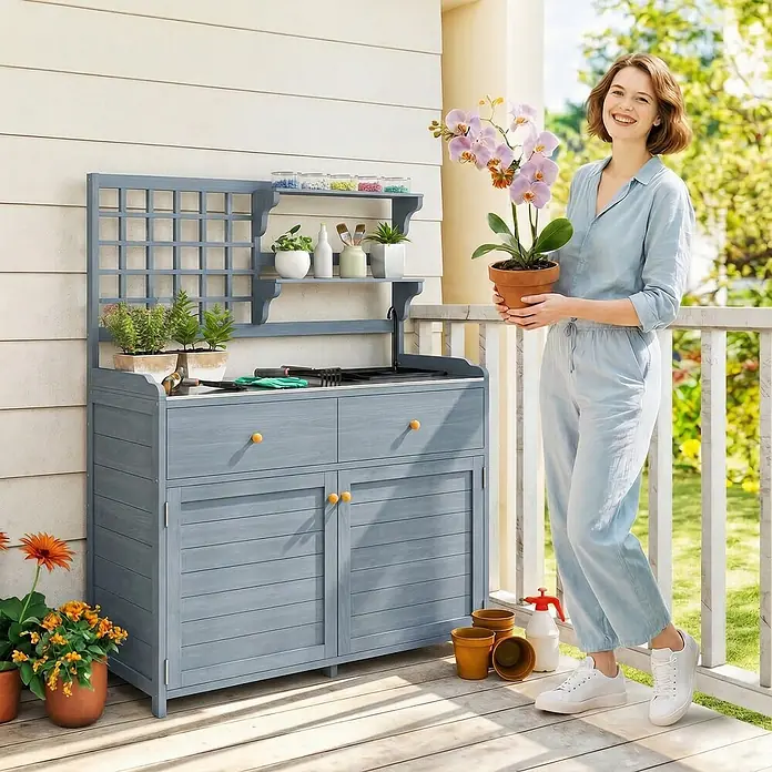 Outsunny Pflanztisch Hellgrau 104L x 44B x 140H cm -  - Graublaue Gartenwerkbank aus Holz mit Regalen, Spüle, Schubladen und Schränken, auf einer Terrasse mit einer Frau, die eine Orchidee hält.