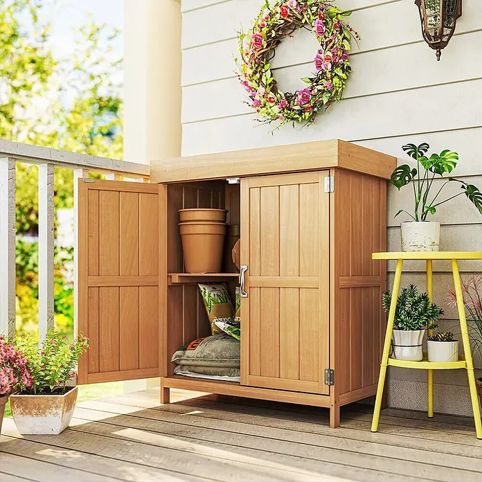 Outsunny Geräteschrank - Außenbreite inkl. Dachüberstand: 74 cm, Außentiefe inkl. Dachüberstand: 43 cm, Holz, Natur - Ein heller Holz-Gartenschrank mit zwei Türen und einem Regal, gefüllt mit Blumentöpfen und Erdsäcken, auf einer Holzveranda neben Topfpflanzen.