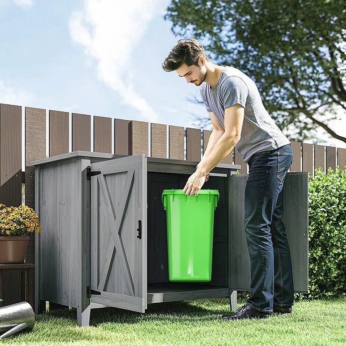 Outsunny Geräteschrank - Außenbreite inkl. Dachüberstand: 110 cm, Außentiefe inkl. Dachüberstand: 60 cm, Holz, Hellgrau - Grauer Holz-Gartenschrank mit Scheunentüren, enthält eine grüne Tonne, von Mann im Garten genutzt.