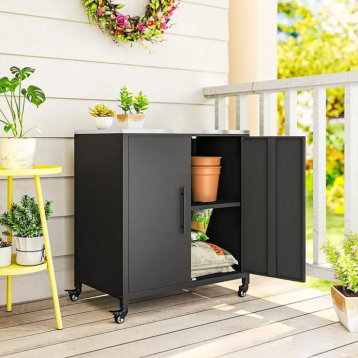 Outsunny Geräteschrank - Außenbreite inkl. Dachüberstand: 80 cm, Außentiefe inkl. Dachüberstand: 50 cm, Metall, Schwarz - Schwarzer Outdoor-Stauraumschrank mit silberner Oberseite und Rollen, geöffnete Tür zeigt Gartenzubehör auf einer Veranda.