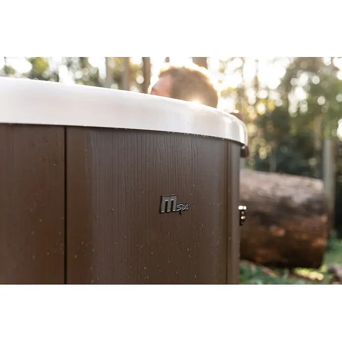 MSpa Mobil-Whirlpool Rowa Frame - Ø x H: 182 x 70 cm, Braun, 970 l - Brauner MSpa Whirlpool mit weißem Rand und Wassertropfen, draußen genutzt. Eine Person ist im Hintergrund sichtbar.
