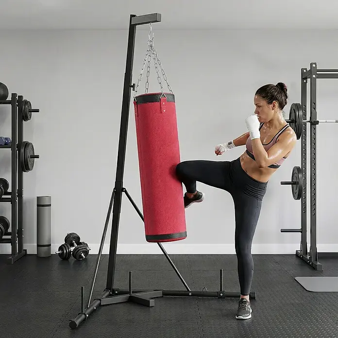 Sportnow Boxsack - Rot - Roter Boxsack an einem schwarzen, freistehenden Ständer, von einer Frau zum Kickboxtraining genutzt.