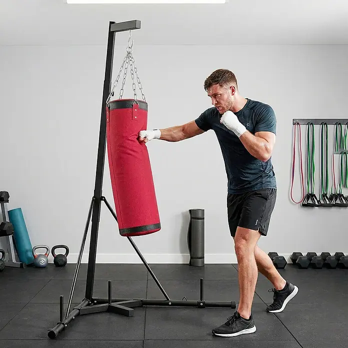 Sportnow Boxsack - Rot - Mann schlägt einen roten Boxsack an einem schwarzen Stand im Fitnessstudio.