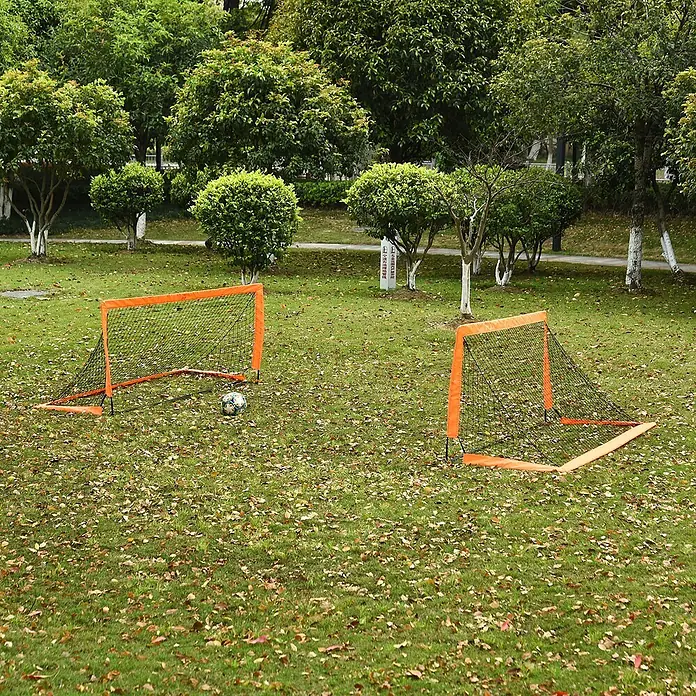 Homcom Fußballtor - Orange, Metall - Zwei tragbare Mini-Fußballtore mit orangefarbenen Rahmen und schwarzen Netzen stehen mit einem Ball auf einer grünen Wiese.