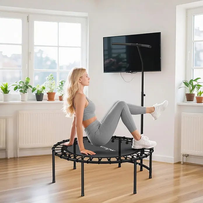 Sportnow Rebounder - Stahl, Schwarz - Frau in grauer Sportkleidung trainiert auf einem schwarzen Minitrampolin mit verstellbarem Haltegriff in hellem Wohnambiente.