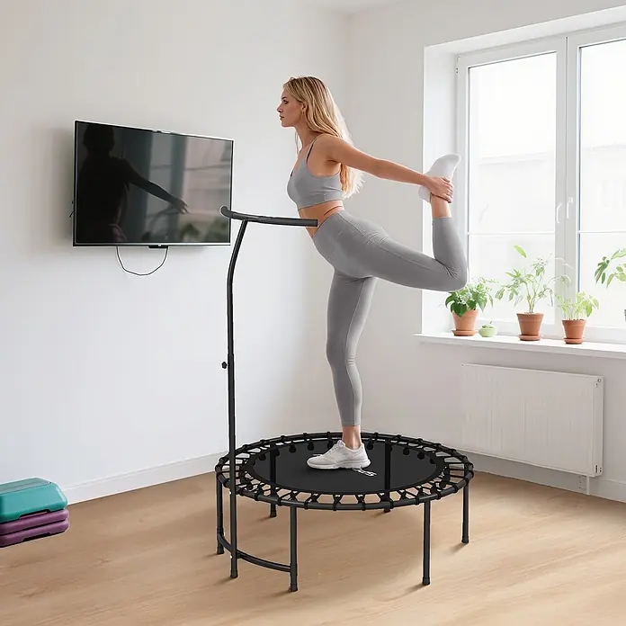 Sportnow Rebounder - Stahl, Schwarz - Frau in grauer Sportkleidung dehnt sich auf schwarzem Rebounder mit Haltegriff.