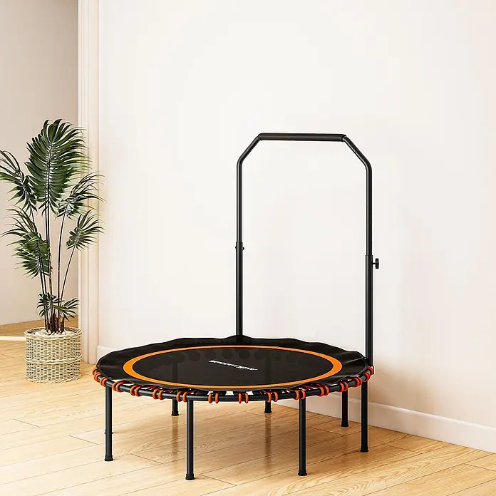 Sportnow Rebounder - Stahl, Schwarz, Orange - Schwarzes Minitrampolin mit orangefarbenen Gummiseilen und Haltegriff auf hellem Holzboden neben einer Topfpflanze.