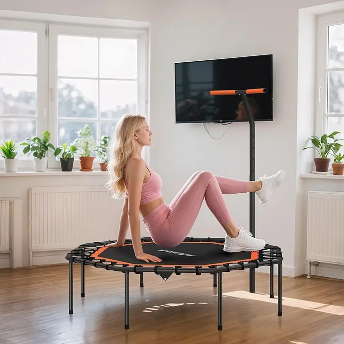 Sportnow Rebounder - Stahl, Schwarz, Orange - Schwarzes und orangefarbenes Fitnesstrampolin mit Haltegriff, von einer Frau zum Training in einem hellen Raum genutzt.