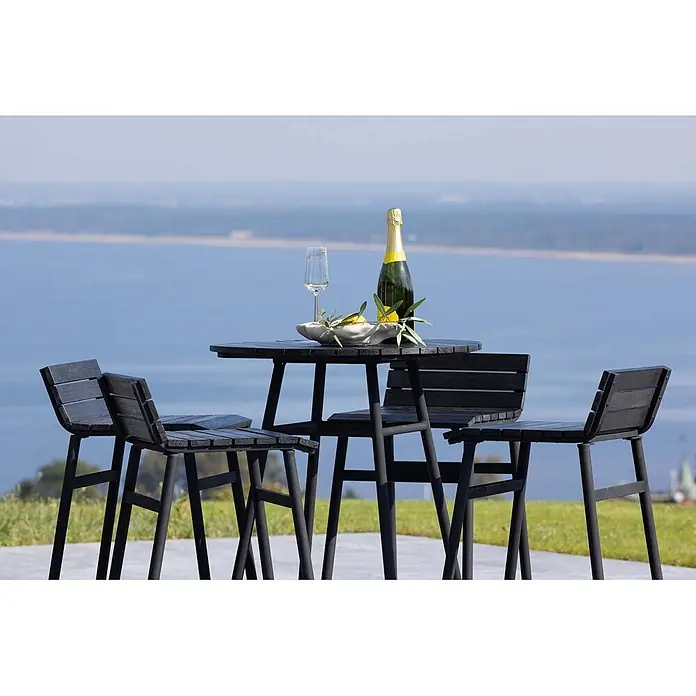 Ebuy24 Gartentisch-Set New Mexico - Gesamtumfang: 5 -tlg., L x B x H: 65 x 65 x 95 cm, Ø x H: 65 x 95 cm, Stahl Akazie, Stapelbar - Schwarzer Outdoor-Bartisch mit vier Hockern vor malerischer Meereskulisse, Sekt auf dem Tisch.