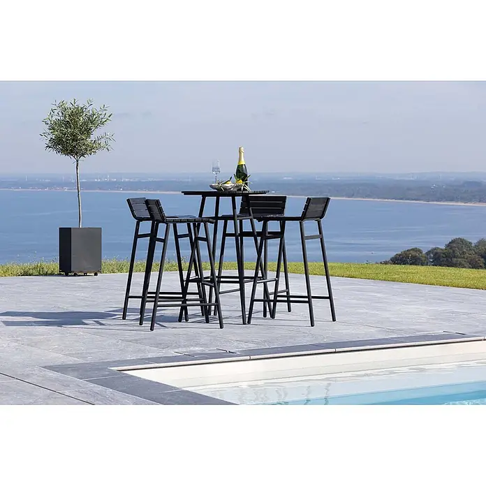 Ebuy24 Gartentisch-Set New Mexico - Gesamtumfang: 5 -tlg., L x B x H: 65 x 65 x 95 cm, Ø x H: 65 x 95 cm, Stahl Akazie, Stapelbar - Schwarzer Outdoor-Bartisch und vier Barhocker auf einer Terrasse am Pool mit Blick auf eine Wasserlandschaft.