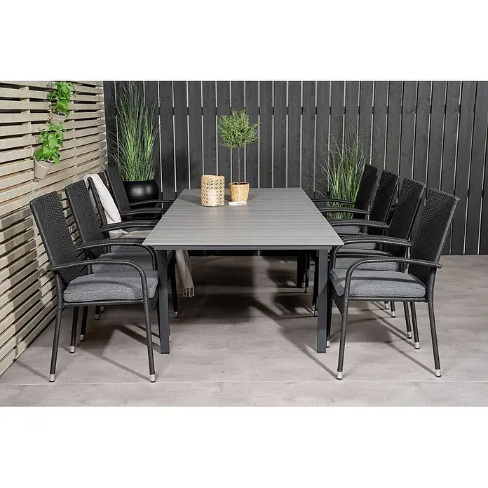 Ebuy24 Gartentisch-Set Levels - Gesamtumfang: 9 -tlg., L x B x H: 160 x 100 x 75 cm, Ø x H: 100 x 75 cm, Rattan, Stahl Aintwood, Aluminium, Stapelbar - Moderne Outdoor-Essgruppe mit grauem Lattenrosttisch und schwarzen Geflechtstühlen mit passenden grauen Kissen, auf einer Terrasse arrangiert.