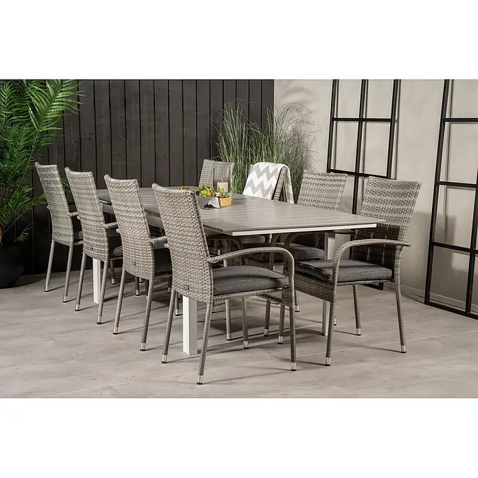 Ebuy24 Gartentisch-Set Levels - Gesamtumfang: 9 -tlg., L x B x H: 100 x 160 x 75 cm, Ø x H: 100 x 75 cm, Rattan, Stahl Aintwood, Aluminium, Stapelbar - Graues Outdoor-Essgruppe mit Geflechtsesseln, dunklen Polstern und einem hellgrauen Tisch, auf einer Terrasse platziert.