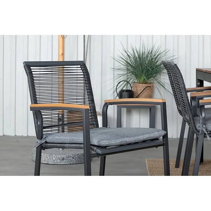 Ebuy24 Gartentisch-Set Bois - Gesamtumfang: 7 -tlg., L x B x H: 205 x 90 x 76 cm, Ø x H: 90 x 76 cm, 100 % Polyester, Holz, Rattan, Stahl Akazie, Aluminium, Stapelbar - Dunkelgrauer Outdoor-Stuhl mit Holzarmlehnen, Seilrücken und hellgrauem Kissen auf einer Terrasse.