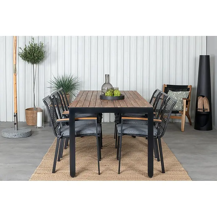 Ebuy24 Gartentisch-Set Bois - Gesamtumfang: 7 -tlg., L x B x H: 205 x 90 x 76 cm, Ø x H: 90 x 76 cm, 100 % Polyester, Holz, Rattan, Stahl Akazie, Aluminium, Stapelbar - Outdoor-Essgruppe: ein Holztisch mit schwarzem Rahmen und sechs Stühlen mit schwarzem Seilgeflecht und grauen Kissen, auf einem Teppich in einer Terrasse.