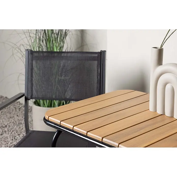 Ebuy24 Gartentisch-Set Holmbeck - Gesamtumfang: 3 -tlg., L x B x H: 70 x 88 x 74 cm, Ø x H: 88 x 74 cm, Textil Akazie, Stapelbar - Gartentisch mit Naturholzlatten und schwarzem Metallgestell, daneben ein passender Stuhl mit schwarzem Netzgewebe auf einer Terrasse.