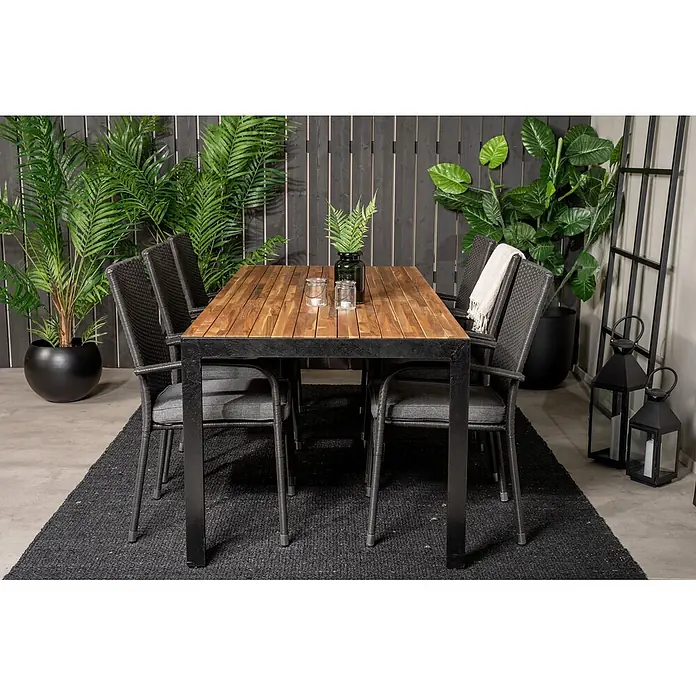 Ebuy24 Gartentisch-Set Bois - Gesamtumfang: 7 -tlg., L x B x H: 205 x 90 x 76 cm, Ø x H: 90 x 76 cm, Rattan, Stahl Akazie, Aluminium, Stapelbar - Gartengarnitur mit rechteckigem Holztisch und sechs dunkelgrauen Korbstühlen mit Kissen, auf einem Teppich im Terrassenbereich.