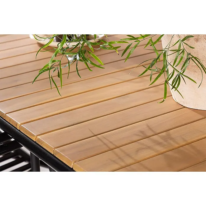 Ebuy24 Gartentisch-Set Holmbeck - Gesamtumfang: 7 -tlg., L x B x H: 200 x 90 x 75 cm, Ø x H: 90 x 75 cm, Akazie Stahl Aluminium, Stapelbar - Nahaufnahme eines hellbraunen Lattenholztisches mit schwarzem Gestell, darauf grüne Pflanzen und ein Terrakottatopf.