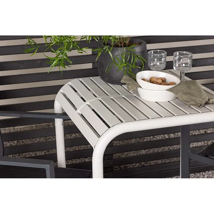 Ebuy24 Gartentisch-Set Borneo - Gesamtumfang: 3 -tlg., L x B x H: 70 x 70 x 75 cm, Ø x H: 70 x 75 cm, Textil Aluminum, Stapelbar - Heller grauer Lamellen-Outdoor-Tisch mit gebogenen weißen Beinen, auf einer Terrasse mit Pflanze und Snacks.
