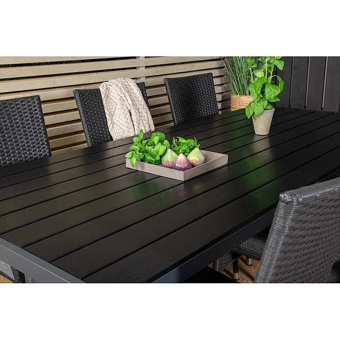 Ebuy24 Gartentisch-Set Break - Gesamtumfang: 7 -tlg., L x B x H: 205 x 90 x 74 cm, Ø x H: 90 x 74 cm, Korbmöbel, Nonwood, Stapelbar - Schwarzer Lamellen-Gartentisch mit dunklem Rahmen, auf einer Terrasse mit Stühlen und Dekoration.