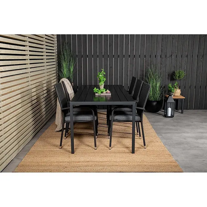 Ebuy24 Gartentisch-Set Break - Gesamtumfang: 7 -tlg., L x B x H: 205 x 90 x 74 cm, Ø x H: 90 x 74 cm, Korbmöbel, Nonwood, Stapelbar - Schwarzer Outdoor-Esstisch mit passenden Stühlen und grauen Kissen auf einem Webteppich für die Terrasse.
