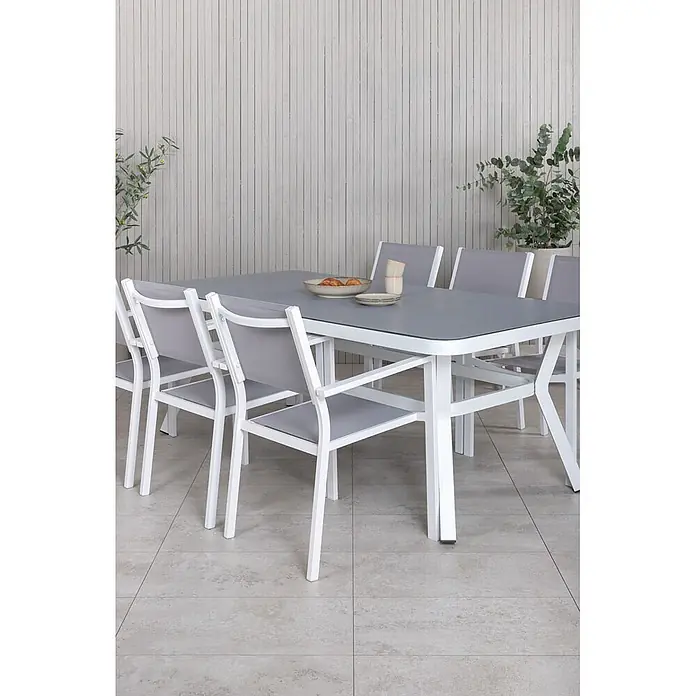 Ebuy24 Gartentisch-Set Virya - Gesamtumfang: 7 -tlg., L x B x H: 100 x 200 x 74 cm, Ø x H: 100 x 74 cm, 100 % PVC, Aluminium Aluminium, Glas, Schnur, Stapelbar - Outdoor-Essgruppe mit grauem Tisch und weiß-grauen Stühlen, für eine Mahlzeit arrangiert.