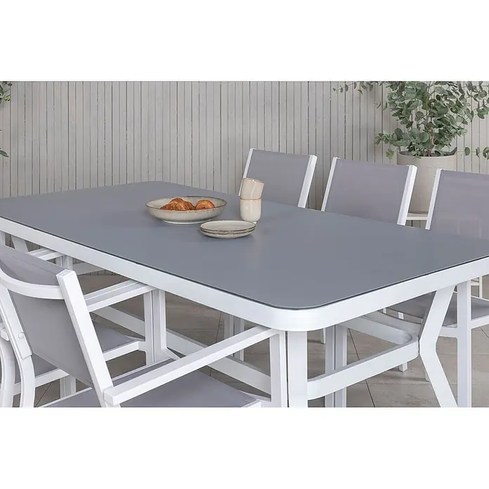 Ebuy24 Gartentisch-Set Virya - Gesamtumfang: 7 -tlg., L x B x H: 100 x 200 x 74 cm, Ø x H: 100 x 74 cm, 100 % PVC, Aluminium Aluminium, Glas, Schnur, Stapelbar - Weißer Gartentisch mit grauer Platte und passenden Stühlen, mit Frühstücksgeschirr.