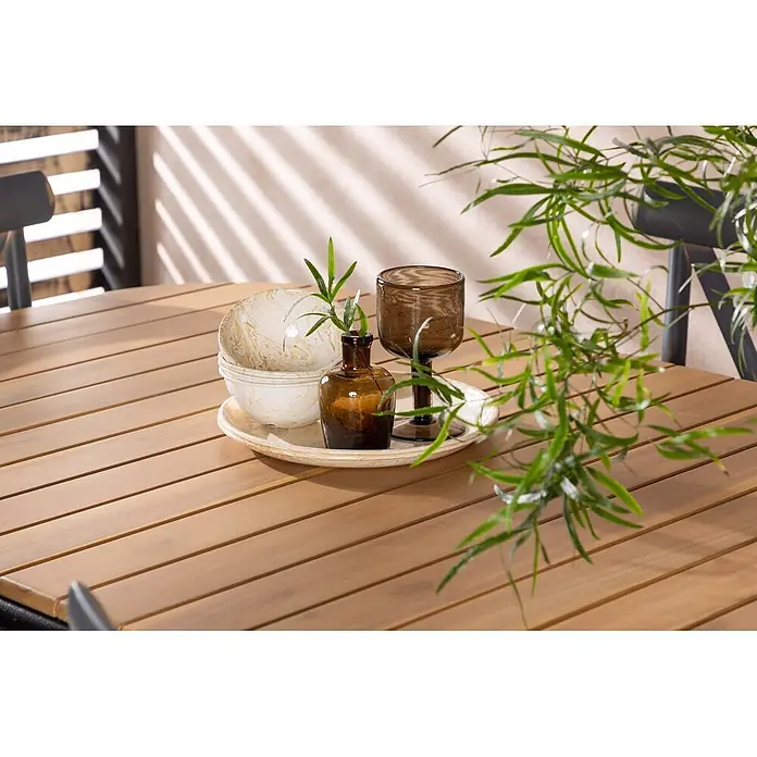 Ebuy24 Gartentisch-Set Holmbeck - Gesamtumfang: 7 -tlg., L x B x H: 90 x 200 x 75 cm, Ø x H: 90 x 75 cm, Aluminium Akazie, Stapelbar - Outdoor-Tisch aus Holzlatten mit Dekotablett und Schalen, auf einer sonnigen Terrasse mit Pflanzen.