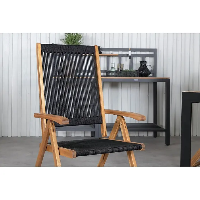 Ebuy24 Gartentisch-Set Bois - Gesamtumfang: 7 -tlg., L x B x H: 90 x 205 x 76 cm, Ø x H: 90 x 76 cm, 100 % Polyester, Akazie Akazie, Aluminium, Stapelbar - Klappstuhl mit hellem Holzrahmen und schwarzer geflochtener Seilbespannung, in einer Terrassenumgebung.