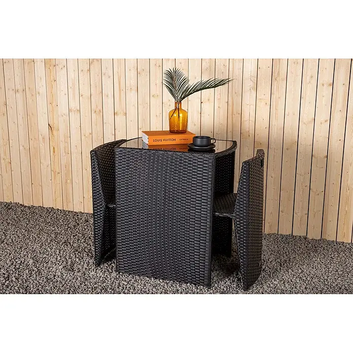 Ebuy24 Gartentisch-Set Savanna - Gesamtumfang: 3 -tlg., L x B x H: 50 x 66 x 75 cm, Ø x H: 50 x 75 cm, Kunststoff, Metall, Ausziehbar - Schwarzes Rattan-Bistro-Set mit Glastisch und zwei Stühlen, ideal für den Außenbereich, auf Kies vor einer Holzwand.