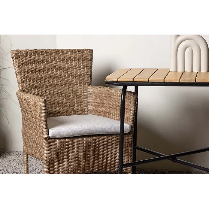 Ebuy24 Gartentisch-Set Holmbeck - Gesamtumfang: 3 -tlg., L x B x H: 70 x 88 x 74 cm, Ø x H: 88 x 74 cm, Aluminium Akazie, Stapelbar - Brauner geflochtener Terrassenstuhl mit hellem Kissen, neben einem Lamellentisch auf Kiesuntergrund.