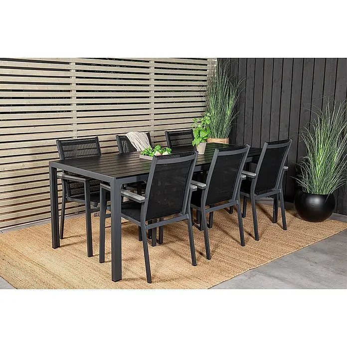 Ebuy24 Gartentisch-Set Break - Gesamtumfang: 7 -tlg., L x B x H: 205 x 90 x 74 cm, Ø x H: 90 x 74 cm, Aintwood Aluminium Textil, Stapelbar - Dunkelgraues Aluminium-Gartenset mit sechs Stühlen aus Netzstoff auf einem geflochtenen Teppich auf einer Terrasse.