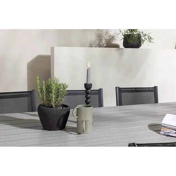 Ebuy24 Gartentisch-Set Garcia - Gesamtumfang: 7 -tlg., L x B x H: 100 x 200 x 74 cm, Ø x H: 100 x 74 cm, Textil Aluminum, Stapelbar - Rosmarinpflanze in schwarzem Topf, gestapelte grüne Tassen und eine brennende graue Kerze in schwarzem Halter auf einem grauen Tisch.