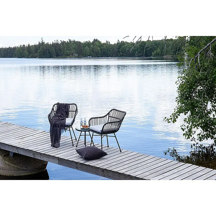 Ebuy24 Loungemöbel-Set Viga - 3 -tlg., Korbmöbel, Schwarz - Schwarze Rattan-Gartenstühle mit grauen Kissen und kleinem Tisch, mit Decke und Kissen auf einem Holzsteg am Seeufer arrangiert.