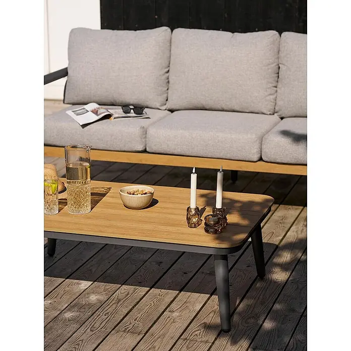 Ebuy24 Loungemöbel-Set Camilla - 4 -tlg., Nonwood (PE), Aluminium, Polyester, Graubeige - Outdoor-Couchtisch mit heller Holzplatte und dunklem Gestell, auf einer Holzterrasse neben einem grauen Sofa mit Getränken und Snacks.