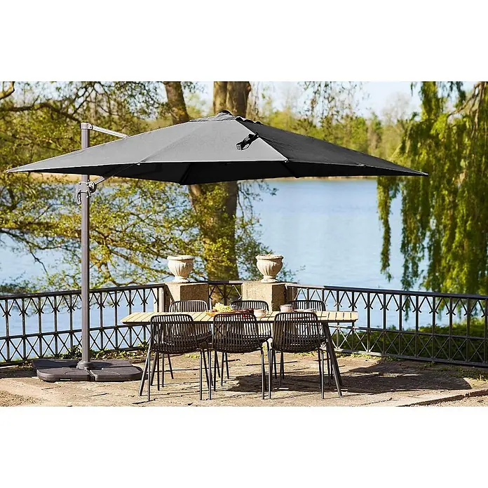 Ebuy24 Marktschirm Bea - Schwarz - Dunkelgrauer Freiarmschirm beschattet Holztisch mit dunklen Stühlen auf einer Terrasse am See.