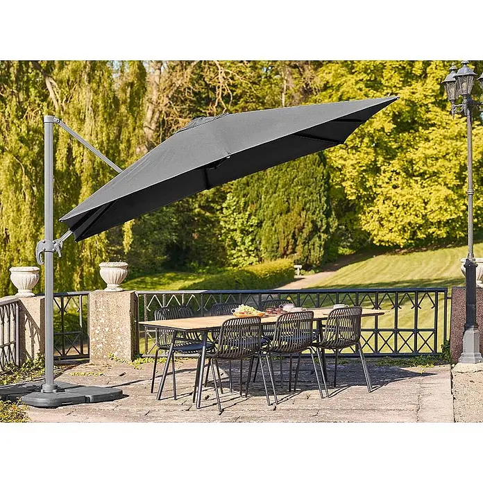 Ebuy24 Marktschirm Bea - Schwarz - Ein grauer Ampelschirm beschattet eine Garten-Essgruppe mit Holztisch und schwarzen Stühlen auf einer Terrasse.