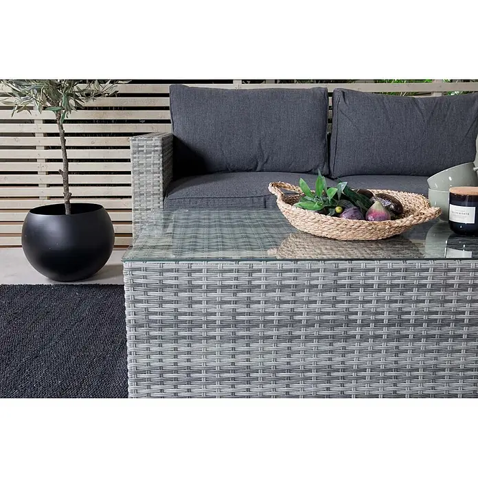 Ebuy24 Loungemöbel-Set Amazon - 2 -tlg., Korbmöbel, Grau - Graue Rattan-Gartensofa mit dunklen Kissen und passendem Glastisch auf Terrasse, dekoriert mit Obstkorb und Pflanze.