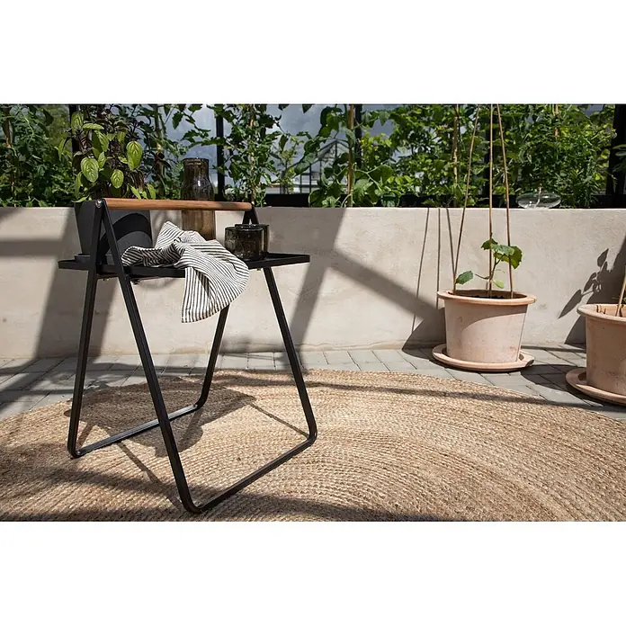 Ebuy24 Garten-Beistelltisch Clarin - L x B x H: 45 x 45 x 59 cm, Stahl, Teak, Stapelbar, Sonstige, Schwarz - Schwarzer Metall-Beistelltisch mit Holzgriff, draußen auf einer Terrasse mit einer Pflanze.