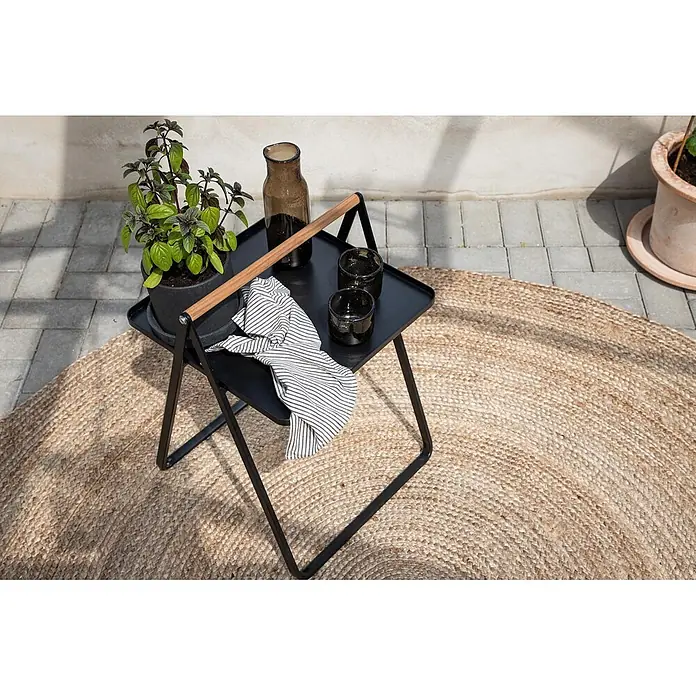 Ebuy24 Garten-Beistelltisch Clarin - L x B x H: 45 x 45 x 59 cm, Stahl, Teak, Stapelbar, Sonstige, Schwarz - Schwarzer Beistelltisch aus Metall mit Holzgriff, draußen auf Juteteppich mit Pflanze und Trinkgläsern arrangiert.